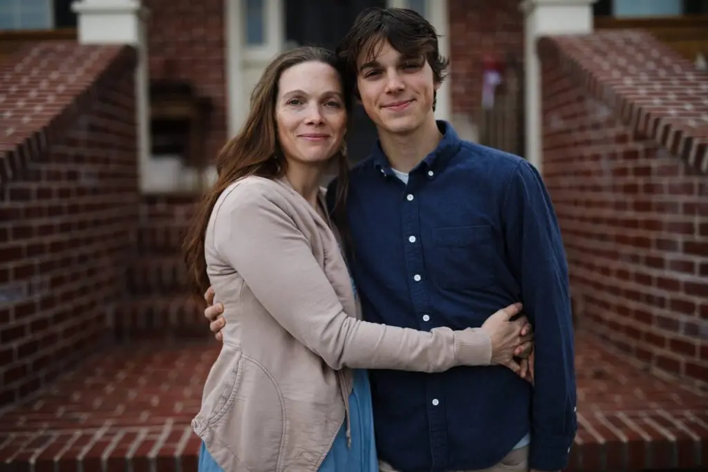 a woman in a tan sweater holding her adult son. They are smiling.