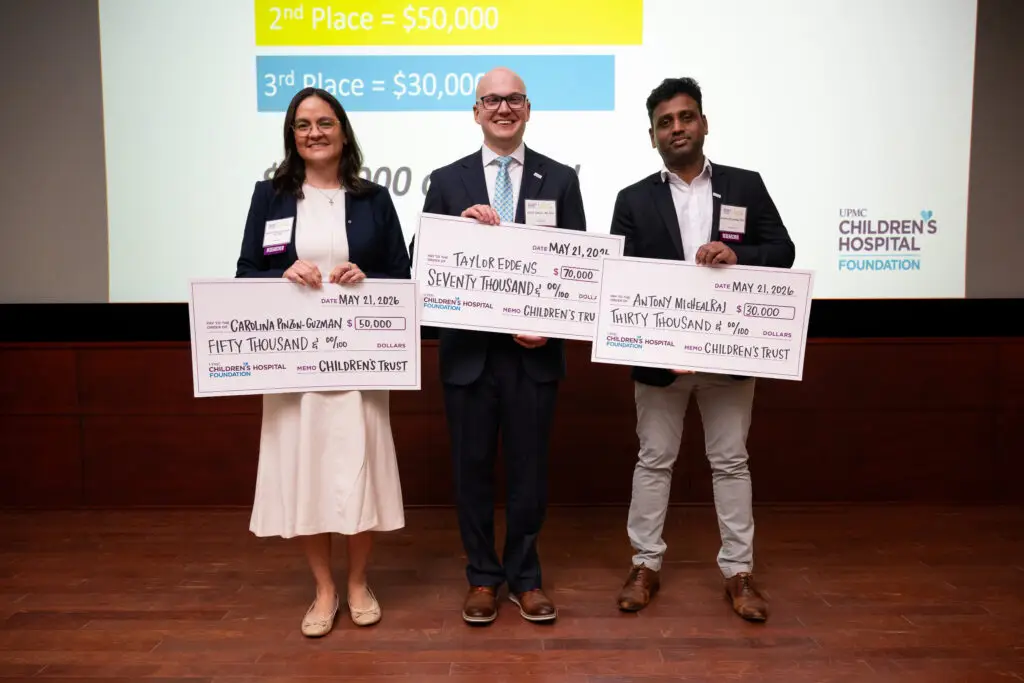 Three researchers stand side-by-side, each holding a large check