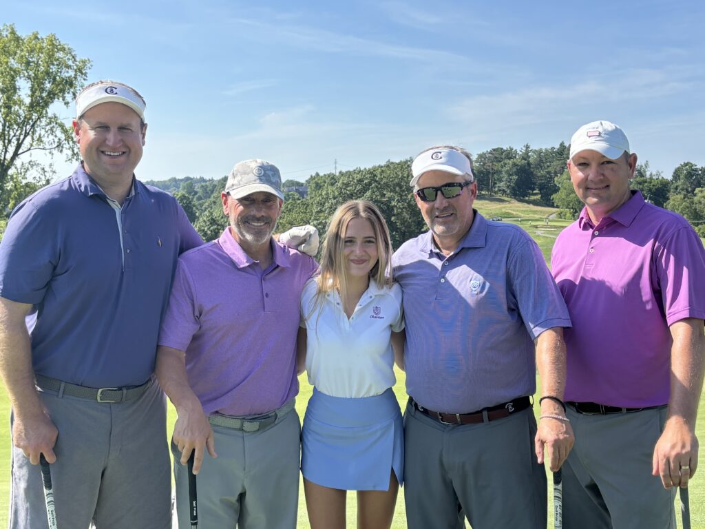 A group of five golfers stand in a line smiling on the golf course