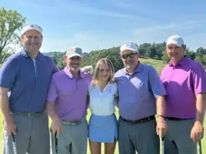A group of five golfers stand in a line smiling on the golf course
