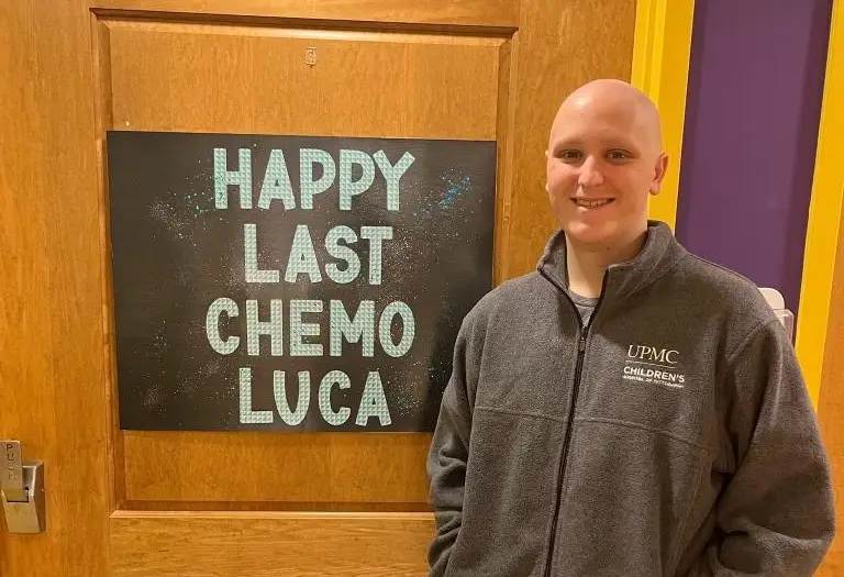 Luca smiling in front of a sign that reads "Happy Last Chemo Luca"