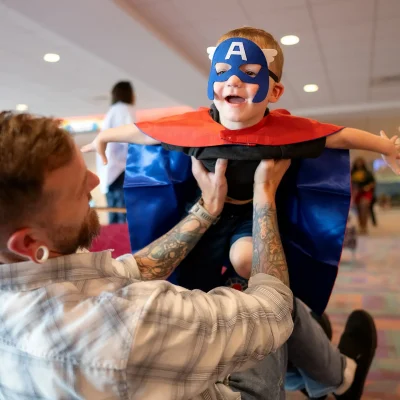 a boy dressed as a superhero pretending to fly while his father holds him up
