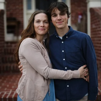 a woman in a tan sweater holding her adult son. They are smiling.